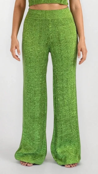 Woman wearing green knitted flare pants. White/grey background.