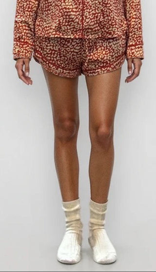 Woman wearing a red and gold leopard print pajama shorts. White/grey background.