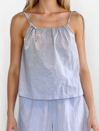 Woman wearing a light blue and pink striped top with tie straps and matching flow bottoms. White/Grey background.