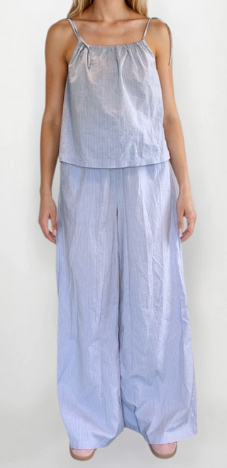 Woman wearing a blue and pink stripe top with tie straps and matching flowy bottoms. White/grey background.