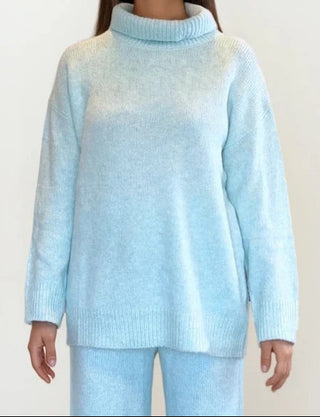 Woman wearing light blue turtleneck and matching knit pants. White/grey background.