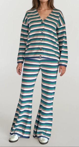 Woman wearing a pink, white, blue and green striped button up sweater cardigan with matching flared sweater pants. White/grey background.