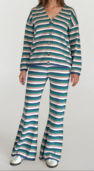 Woman wearing a white, pink, blue, green stripe button up cardigan with matching flare bottom pants. White/grey background.