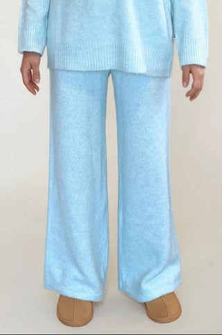 Woman wearing light blue knit pants. White/grey background.