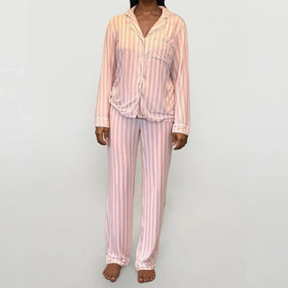 Person wearing long sleeve, long bottom pink and white striped pajama set on a plain grey background